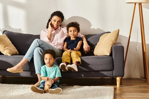 Fröhliche afrikanisch-amerikanische Mutter verbringt Zeit mit ihren Söhnen vor dem Fernseher im heimischen Wohnzimmer — Stockfoto