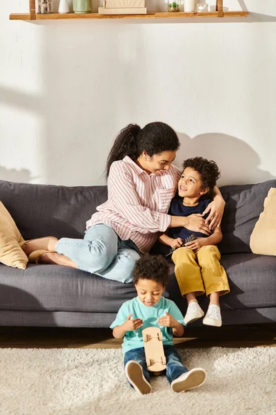 Радостная африканская американская мать сидит и смотрит фильмы со своими очаровательными сыновьями в гостиной дома — стоковое фото