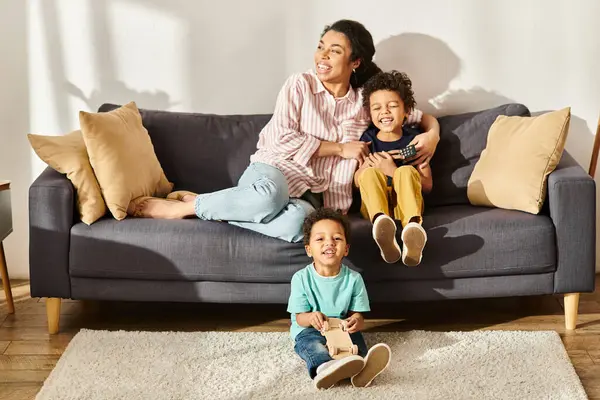 Jolly african american boy playing wooden toy car next to his mother and brother sitting on sofa — Stock Photo
