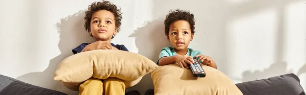 Adorables garçons afro-américains assis sur un canapé avec des oreillers et regarder des films intéressants — Photo de stock