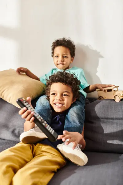 Joyeux afro-américains mignons garçons tenant télécommande et voiture jouet en bois et regarder des films — Photo de stock