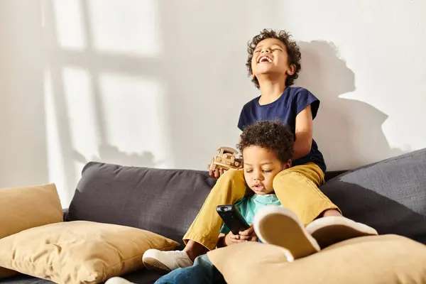 Alegres irmãos afro-americanos brincando com brinquedo de carro e assistindo TV na sala de estar — Fotografia de Stock