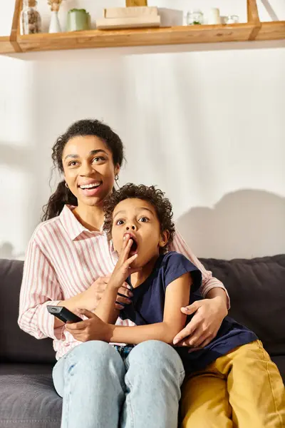 Alegre afroamericana madre y su impactado pequeño hijo viendo interesante película en casa - foto de stock