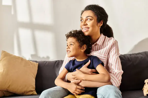 Joyous african american mother and he little son hugging on sofa and looking away, modern parenting — Stock Photo