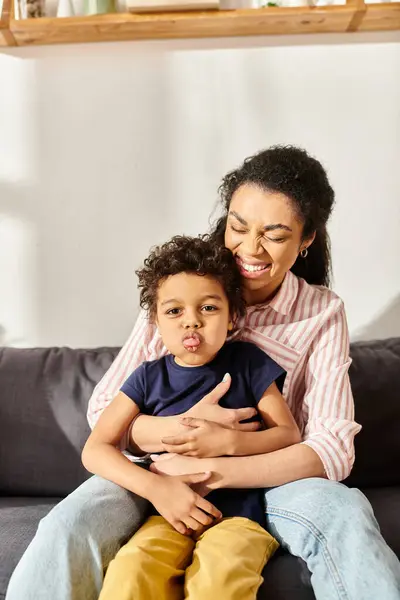 Alegre afroamericana mujer sosteniendo su pequeño adorable hijo que sobresale lengua a cámara - foto de stock