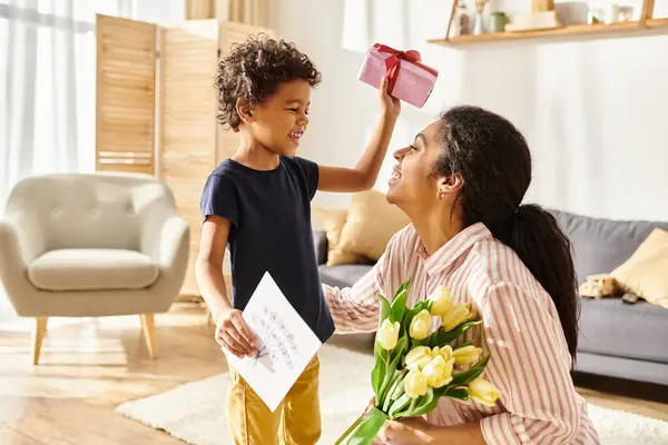 Adorable garçon afro-américain donnant cadeau et carte postale à sa mère joyeuse, parentalité moderne — Photo de stock