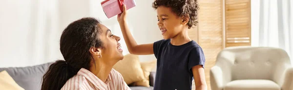 Cute african american boy giving present and postcard to his jolly mother, modern parenting, banner — Stock Photo