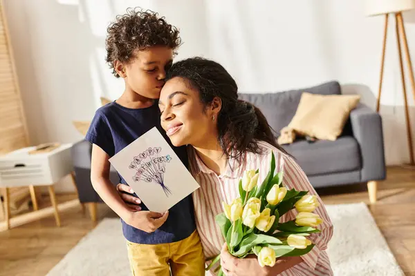 Cheerful african american woman holding postcard and tulips and hugging her son, Mothers day — Stock Photo