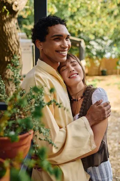 An interracial couple shares a loving hug in front of a majestic tree in a serene natural setting. — Stock Photo