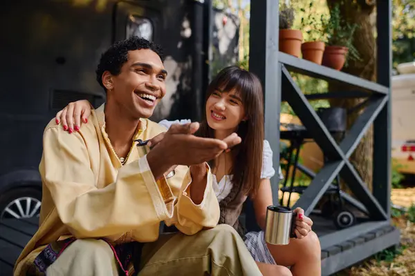 An interracial couple sits on the ground, pointing excitedly at something in front of them, immersed in the beauty of nature. — Stock Photo