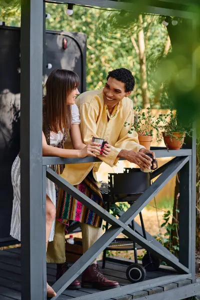 A man and woman, an interracial couple, sit relaxed on a porch, surrounded by nature, sharing a moment of peace and connection. — Stock Photo