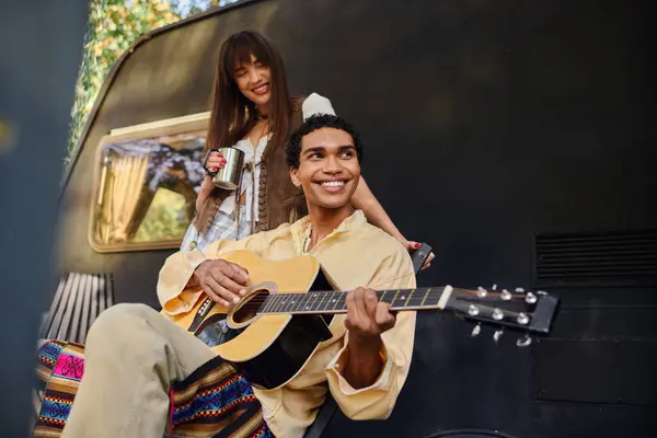 Ein Mann bringt einer Frau ein Ständchen mit akustischer Gitarrenmusik am knisternden Lagerfeuer in einem ruhigen Ambiente im Freien. — Stockfoto