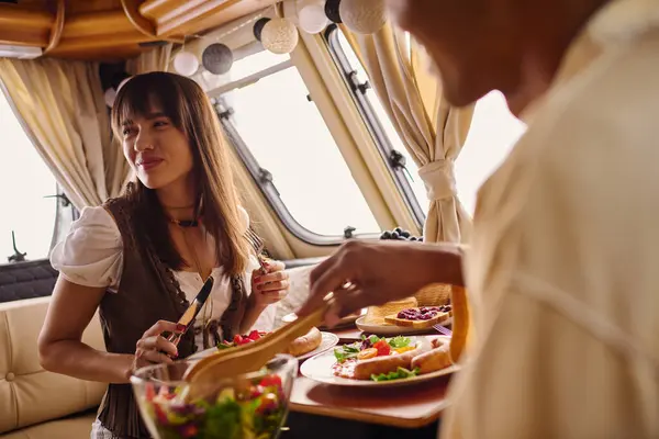 Eine farbige Frau serviert einem Mann im Lieferwagen gnädig eine Mahlzeit, während sie einen romantischen Kurzurlaub genießen — Stockfoto