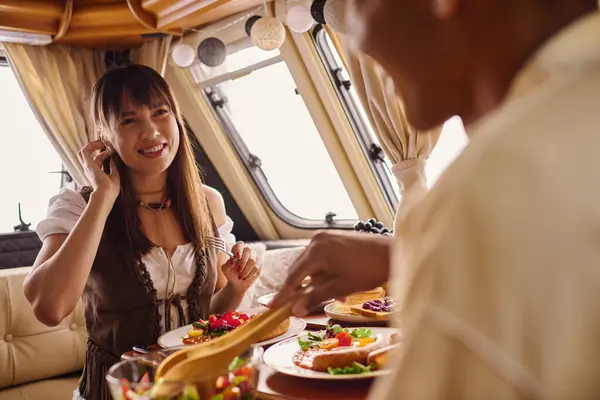 An interracial couple enjoys a romantic lunch in a camper van, savoring a delicious meal together at a cozy table. — Stock Photo
