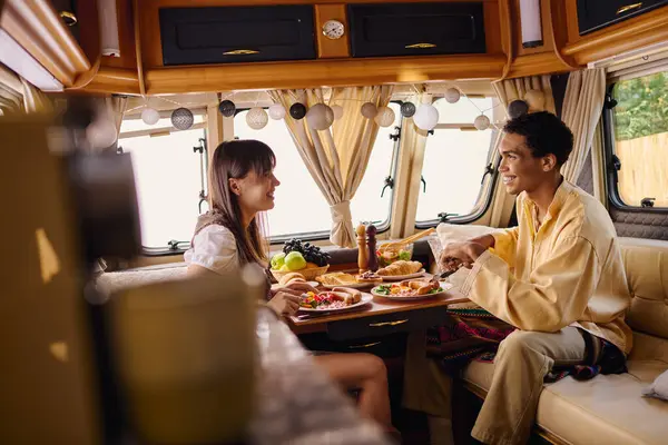 A man and a woman of different races enjoy a romantic lunch together inside a camper van during their travels. — Stock Photo