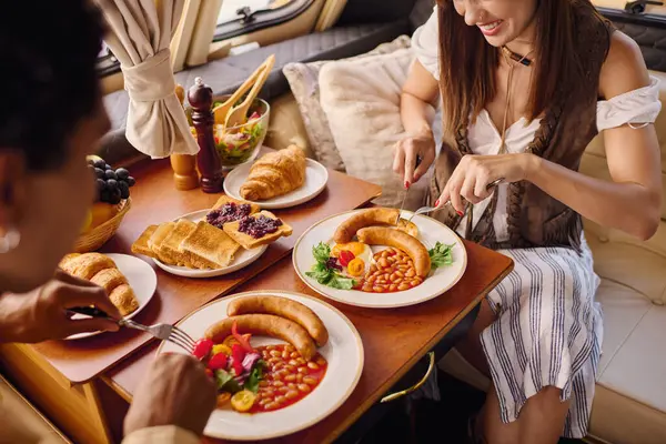 Une femme s'assoit à une table, dégustant une variété de délicieux plats étalés devant elle lors d'une escapade romantique dans un camping-car. — Photo de stock