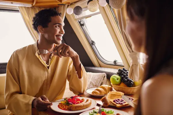 An interracial couple indulging in a delightful lunch inside a camper van, creating a romantic ambiance. — Stock Photo