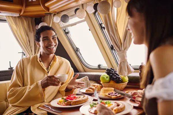 An interracial couple enjoys a delicious meal together in a camper van, creating memories on a romantic getaway. — Stock Photo