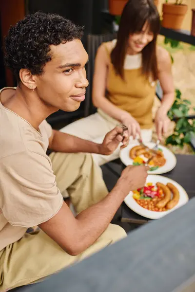 Un couple interracial dégustant un repas ensemble sur un banc, entouré d'un cadre confortable camping-car. — Photo de stock