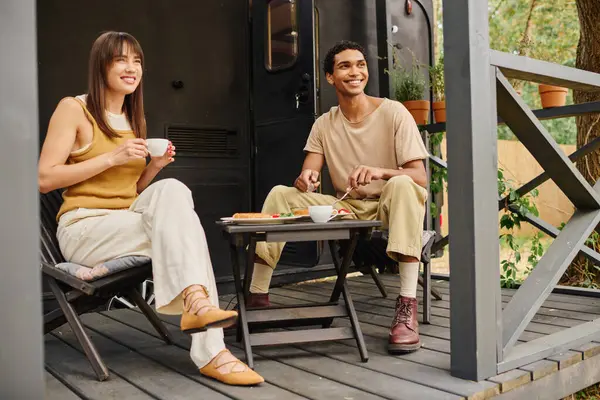 Un couple interracial se détend ensemble sur un porche confortable, en profitant de l'autre compagnie dans un cadre paisible. — Photo de stock