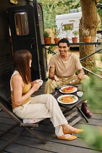 Un couple interracial profite d'un délicieux repas, assis sur une terrasse dans un camping-car lors d'une escapade romantique. — Photo de stock