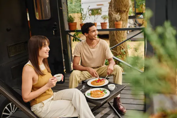 An interracial couple enjoying a meal together on a porch with a camper van in the background. — Stock Photo