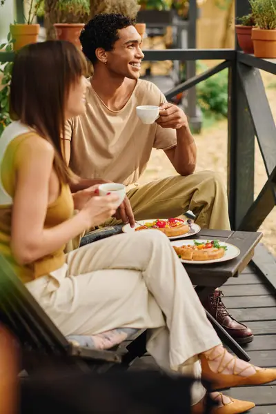 Ein gemischtrassiges Paar sitzt auf einer Veranda und isst zusammen in einem friedlichen und romantischen Moment während ihres Reiseaufenthalts.. — Stockfoto