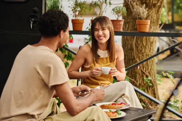 Um casal interracial sentado em uma mesa, desfrutando de uma refeição juntos em uma van de campista acolhedora durante uma escapadela romântica. — Fotografia de Stock