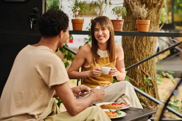 An interracial couple seated at a table, enjoying a meal together in a cozy camper van during a romantic getaway. — Stock Photo