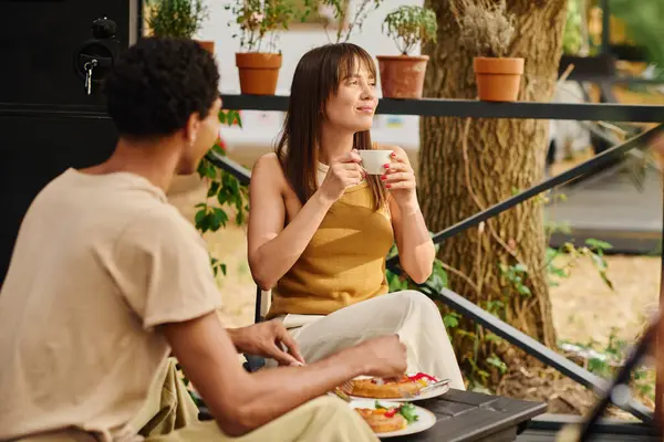 Un hombre y una mujer disfrutan de un momento tranquilo en un banco, saboreando tazas de café en compañía de los demás. - foto de stock