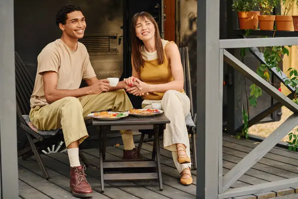 Un uomo e una donna di razze diverse sono seduti pacificamente su un portico, godendosi reciprocamente la compagnia in un ambiente tranquillo. — Foto stock