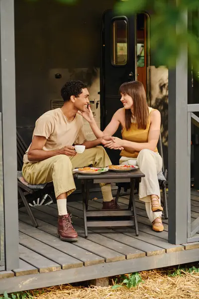 Una coppia interrazziale si gode un delizioso pasto insieme a un tavolo all'aperto, immersi nella natura e nel caldo abbraccio dell'amore. — Foto stock