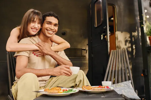 A man and a woman enjoy a peaceful moment on a bench in front of a van, soaking in the scenery. — Stock Photo