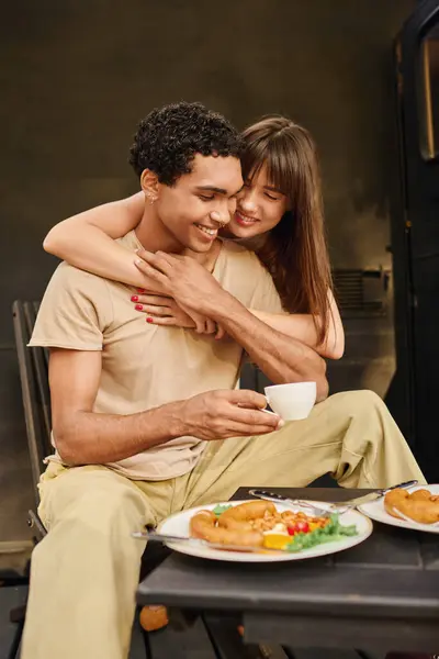 An interracial couple enjoying a delicious meal together at a table in a cozy camper van during a romantic getaway. — Stock Photo