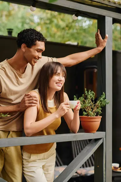 A man and woman, an interracial couple, stand on a porch, enjoying a moment together on their romantic getaway. — Stock Photo
