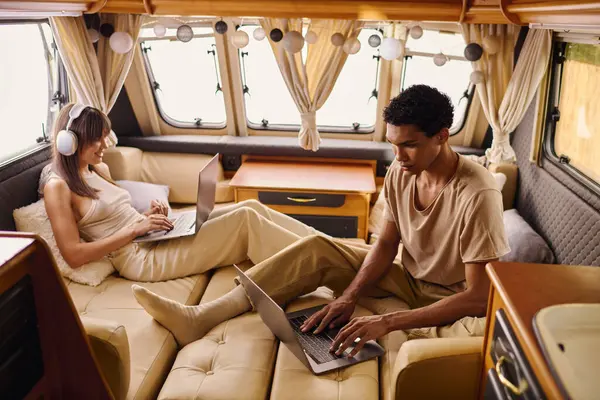 Um homem e uma mulher sentam-se em um sofá, cada um absorvido em seus laptops, com expressões focadas. — Fotografia de Stock