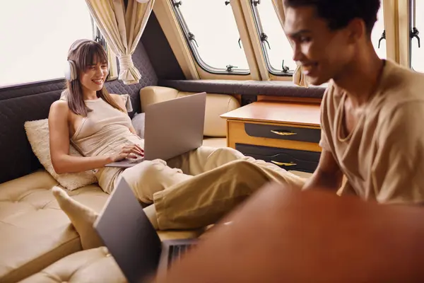 A multicultural couple relaxes on a sofa with a laptop, engaged in online activities. — Stock Photo