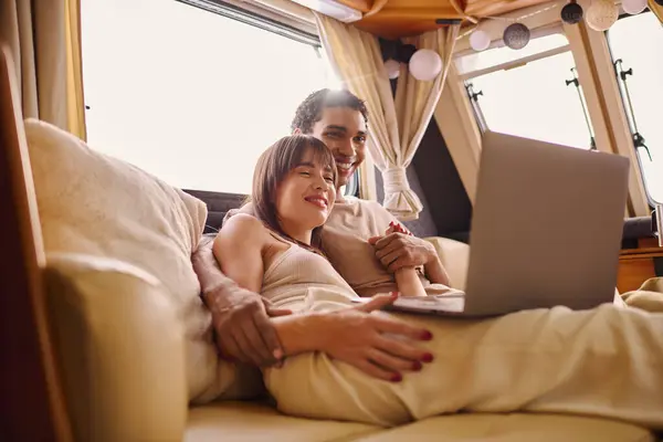 Un uomo e una donna si siedono strettamente su un divano, entrambi concentrati su uno schermo del computer portatile di fronte a loro. — Foto stock