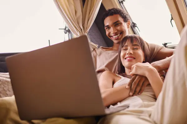 Coppia interrazziale sedersi sul letto, assorto nello schermo del computer portatile in camper moderno — Foto stock