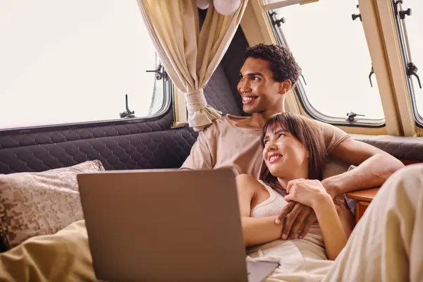 Un uomo e una donna si siedono su un letto, concentrati su uno schermo portatile, condividendo un momento di connessione nel mondo digitale. — Foto stock