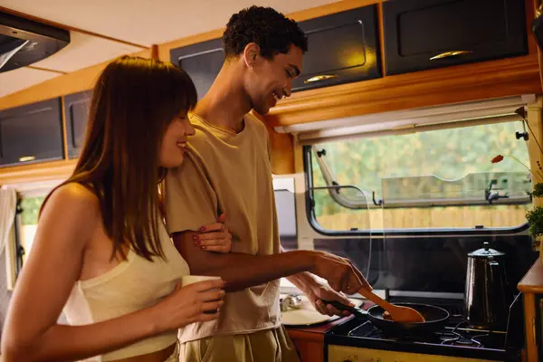 An interracial couple is joyfully preparing a meal together inside a cozy camper van. — Stock Photo