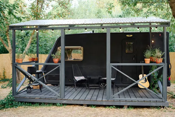 A small black trailer with a guitar on the porch, set against a serene backdrop, evokes a cozy musical moment — Stock Photo
