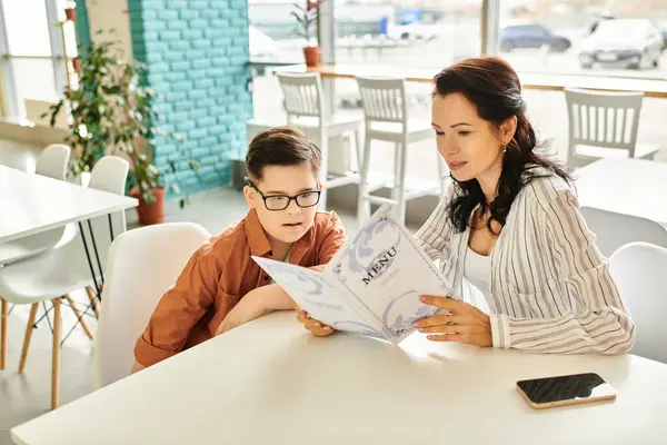 Bela mãe em traje casual olhando para o menu no café com seu filho inclusivo com síndrome de Down — Fotografia de Stock