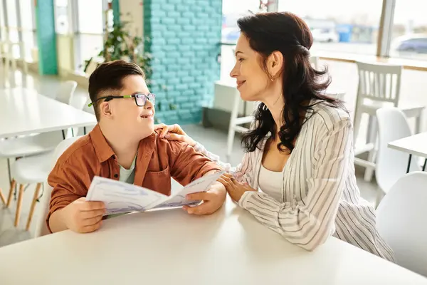 Mãe alegre amoroso sentado no café com seu filho inclusivo com síndrome de Down com óculos e menu — Fotografia de Stock