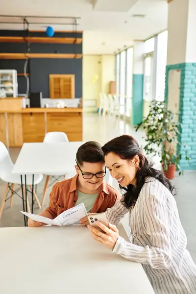 Beautiful woman in casual clothes in cafe with her inclusive son with Down syndrome holding menu — Stock Photo