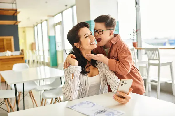 Привлекательная веселая мать в повседневной одежде со своим инклюзивным сыном с синдромом Дауна — стоковое фото