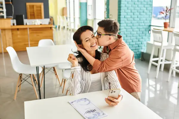 Attractive merry mother in casual clothes with her inclusive son with Down syndrome, kiss in cheek — Stock Photo