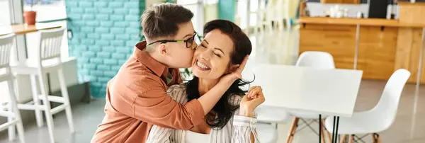 Люблячий син з синдромом Дауна цілує свою щасливу матір в кафе, горизонтальний банер — стокове фото