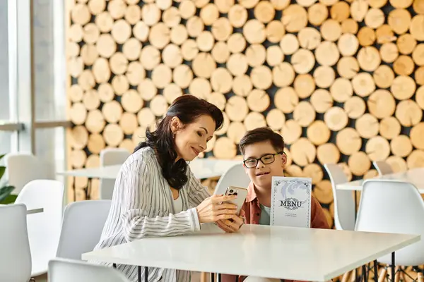 Cheerful woman in cozy clothes with her son with Down syndrome looking at menu on smartphone — Stock Photo