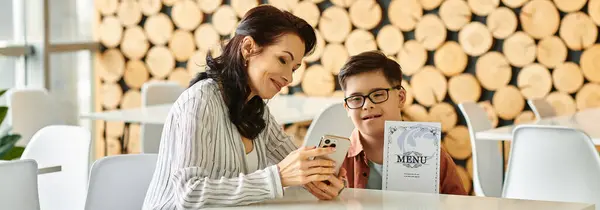 Mulher alegre em roupas acolhedoras com seu filho com síndrome de Down olhando para o menu no smartphone, banner — Fotografia de Stock
